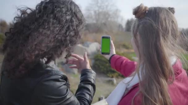 Sparando alle spalle del giovane uomo mediorientale e donna caucasica tenendo smartphone con schermo verde, parlando e salutando. Giovane coppia felice in chat con la famiglia o gli amici tramite video chat . — Video Stock