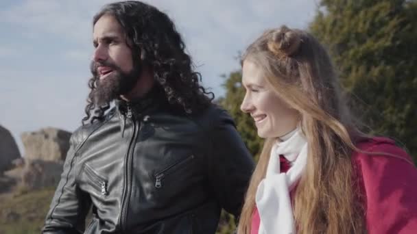 Retrato de cerca de jóvenes hippies parados en el soleado parque otoñal y mirando hacia otro lado. Mujer caucásica y hombre de Oriente Medio con pelo largo rizado citas al aire libre . — Vídeos de Stock