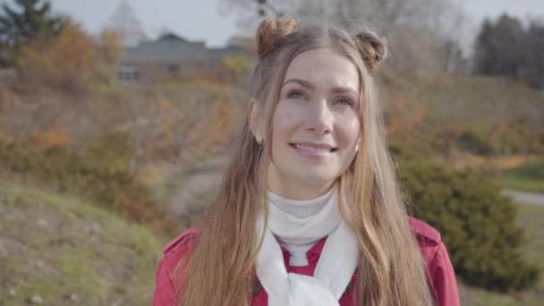 Portret van een jonge blanke vrouw die naar de camera kijkt en glimlacht. Blond mooi meisje in het najaarspark. Gelukkig hippie rustend buiten. — Stockvideo