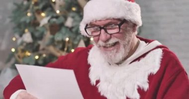 Noel Baba 'nın zarif gözlüklü portresi mektup okuyor ve başını kaşıyordu. Noel Baba, Noel arifesinde çocuk için hediye düşünüyor. Sinema 4k Prores Merkezi.