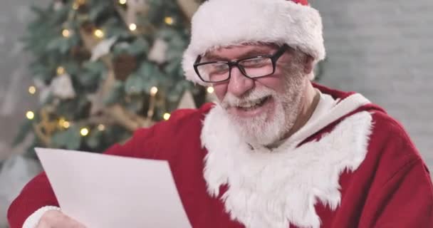 Detailní portrét Santa Clause v elegantních brýlích, jak čte dopis a škrábe se na hlavě. Santa přemýšlí o dárku pro dítě na Silvestra. Cinema 4k Prores Hq. — Stock video