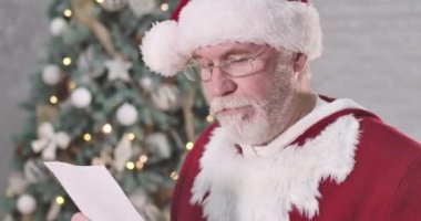Şok olmuş Noel Baba 'nın portresi başka yöne bakıyor. Beyaz sakallı son sınıf öğrencisi çocuk için hangi hediyeyi seçeceğini düşünüyor. Noel ağacının arka planında düşünceli Noel Baba. Sinema 4k Prores Merkezi.