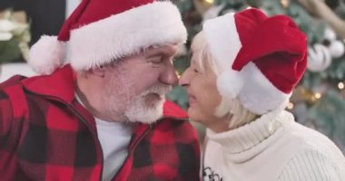 Kameraya bakıp gülümseyen, burunlarını ovuşturan yaşlı beyaz bir çiftin yakın plan portresi. Koca, sevgili karısını burnundan öpüyor. Sonsuz aşk, tatiller, Noel. Sinema 4k Prores Merkezi.