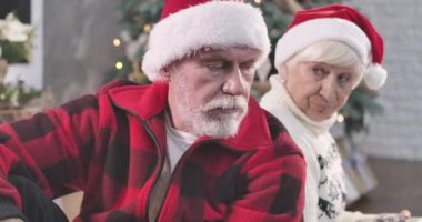 Süslü Noel ağacının arkasında eşiyle sırt sırta oturan yakışıklı beyaz adamın portresi. Mutsuz kadın üzgün kocasına hediye kutusu veriyor. Sinema 4k Prores Merkezi.