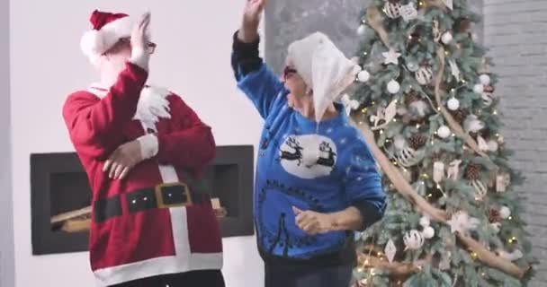 Positive senior Caucasian man and woman playing clapping game and starting fun dancing. Cheerful couple in 3D glasses having fun in front of Christmas tree. Joy, holidays. Cinema 4k ProRes HQ. — стокове відео