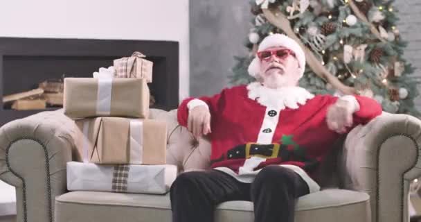 Hombre caucásico de edad avanzada agotado en Santa Claus sombrero reclinado en el sofá y la firma. Viejo cansado con barba blanca descansando en la habitación con árbol de Navidad y cajas de regalo. Sede del cine 4k ProRes . — Vídeo de stock