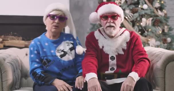 Retrato de alegre pareja de ancianos caucásicos viendo películas en 3D. Esposo y esposa en ropa de Navidad sentados en el sofá al fondo del árbol de Año Nuevo. Los cónyuges felices se divierten. Sede del cine 4k ProRes . — Vídeo de stock