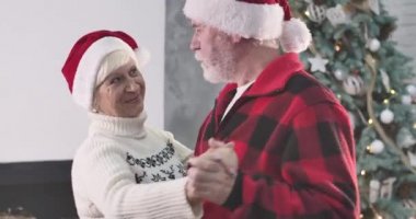 Beyaz sakallı, olgun beyaz bir adamın yeni yıl arifesinde evde karısıyla dans edişinin yakın çekimi. Koca, güzel eşiyle konuşuyor ve gülümsüyor. Noel, tatiller, sonsuz aşk. Sinema 4k Prores Merkezi