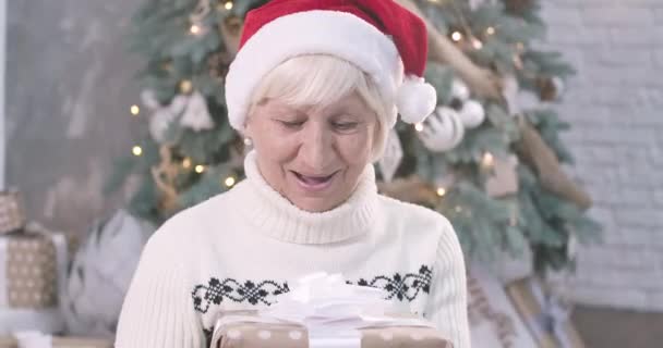 Gezicht van een verbaasde volwassen blanke vrouw met een kerstgeschenkdoos, kijkend naar de camera en glimlachend. Aangename dame die oudejaarsavond thuis doorbrengt. Bioscoop 4k Prores Hq. — Stockvideo