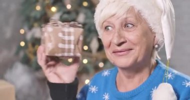 Kafkasyalı olgun bir kadının küçük hediye kutusunu sallamasına şaşırmış yüz ifadesi. Yeni yıl arifesinde meraklı yaşlı bir kadının portresi. Noel arifesi, tatiller. Sinema 4k Prores Merkezi.