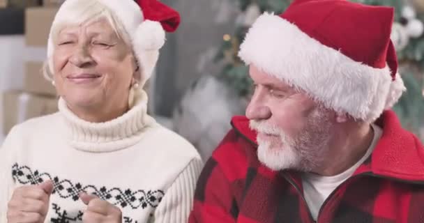 Close-up van positief Kaukasisch oud koppel dat met gesloten ogen onder de kerstboom zit. Man en vrouw die wensen doen op oudejaarsavond. Hoop, vakantie, feest. Bioscoop 4k Prores Hq. — Stockvideo