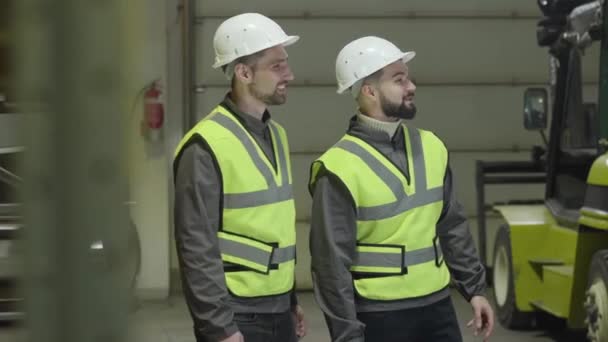 Retrato de perfil de dois homens caucasianos em pé no armazém e conversando. Empregados que trabalham no local de produção. Instalação, fabrico, profissão, profissão . — Vídeo de Stock