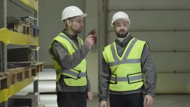 Dos hombres caucásicos de pie en el almacén, hablando y haciendo gestos. Planificación de los trabajadores en el lugar de producción. Planta, fabricación, profesión, ocupación . — Vídeo de stock