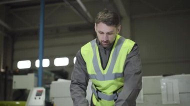 Çelik levha ölçen beyaz eldivenli ve yelekli bir adamın ön görüntüsü. Üretim alanında çalışan kendine güvenen bir profesyonel. Çelik fabrikası, imalat, metal üretim alanı.