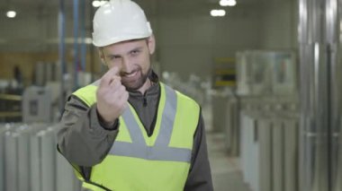 Koruyucu miğfer takmış neşeli beyaz sakallı adam çelik metal boruların arkasında dans ediyor. Çalışan, iş yerinde tatilde eğleniyor. Üretim, çelik endüstrisi.