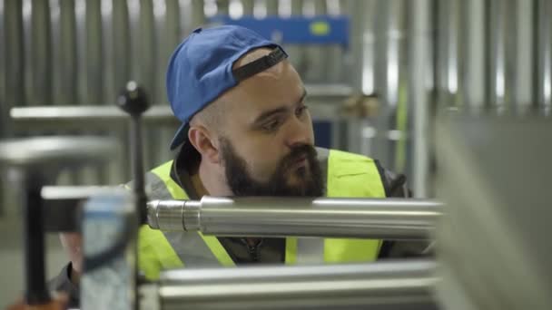 Camera approaching face of serious Caucasian bearded man adjusting steel production equipment. Metal pipes production, steel industry, manufacture. — Stock Video