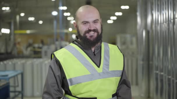 Portret van een kale blanke man met een baard in een pakhuis, kijkend naar de camera en glimlachend. Gelukkige werknemer op zijn werkplek op de productielocatie. Fabriek, fabriek, industrie, werknemer. — Stockvideo