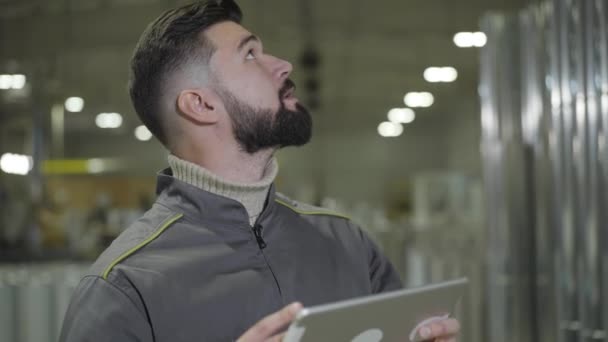 Självsäker kaukasisk ung man kollar in mängden färdig produktion på tillverkningsplatsen. Porträtt av förman som arbetar på stålverket. Tillverkning, industri, lager. — Stockvideo