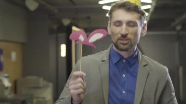 Parti şapkalı gülümseyen beyaz sakallı adamın yakın plan yüzü çalışma alanında şarkı söyleyip dans ediyor. Şirket partisinde eğlenen erkek ofis çalışanının portresi. Boş zaman, eğlence, keyif, mutluluk.