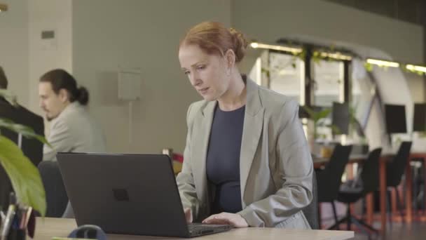 Primer plano de la mujer de mediana edad caucásica concentrada escribiendo en el teclado del ordenador portátil. Retrato de una trabajadora de oficina inteligente en el lugar de trabajo. CEO, gestión, éxito, espacio abierto, coworking . — Vídeo de stock