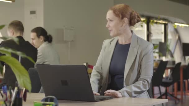 Glada medelålders kaukasiska kvinna sitter på öppen plats kontor, tar på fest hatt och ler. Positiva affärer slady förbereda sig för företagsparti. Kul, nöje, fest, evenemang. — Stockvideo