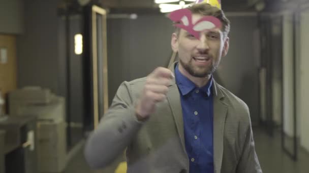 Retrato de un hombre caucásico positivo en traje formal bailando en la oficina. Alegre oficinista masculino en sombrero de fiesta sonriendo y empujando globos. Tipo barbudo divirtiéndose en la fiesta corporativa. Alegría, ocio . — Vídeos de Stock