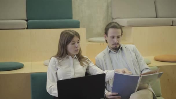 Retrato de trabajadores de oficina masculinos y femeninos creativos discutiendo el proyecto en la oficina de espacio abierto. Joven hombre y mujer caucásicos seguros sentados en innovador coworking y hablando. Negocios, discusión . — Vídeo de stock