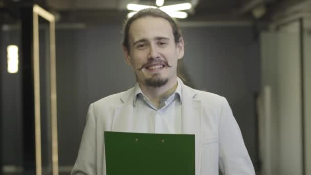 Close-up de homem caucasiano feliz com olhos castanhos e cabelo preto olhando para a câmera e sorrindo. Trabalhador de escritório masculino em pasta de documento de retenção de terno de negócios. CEO, gerente, empresário . — Vídeo de Stock