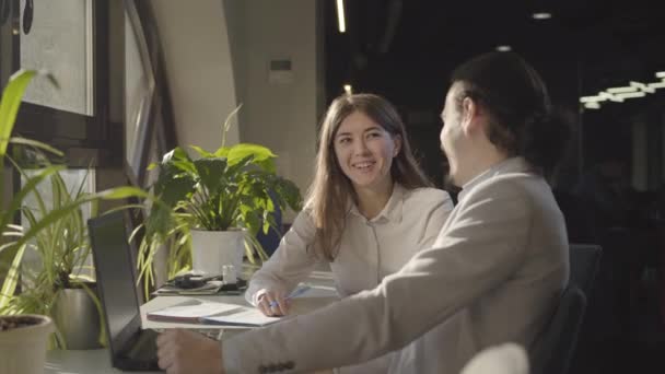 Twee Kaukasische kantoormedewerkers die 's nachts in de open ruimte zitten en het project bespreken. Jongeman en vrouw zitten aan tafel en delen ideeën. Zaken, management, teamwork. — Stockvideo