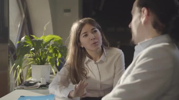 Close-up van de jonge blanke zakenvrouw die 's nachts met een mannelijke collega op kantoor zit te praten. Mooie vrouwelijke kantoormedewerker bespreken zakelijke problemen met collega. Management, teamwork. — Stockvideo