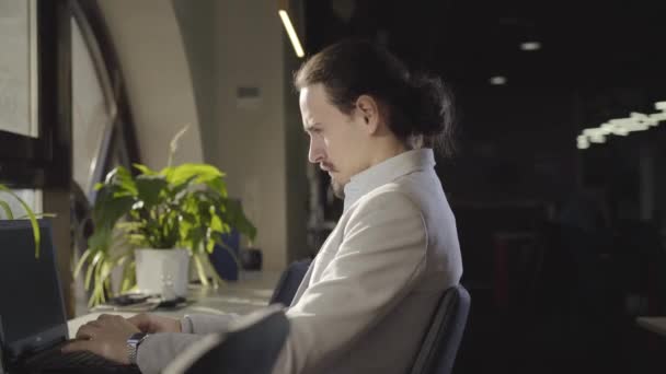 Side view of confident Caucasian man in formal suit sitting in open space at night with laptop. Portrait of CEO at workplace. Business, success, overworking, hardworking. — Stock Video