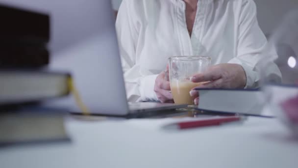 Close-up van volwassen vrouwelijke handen die koffiebeker vasthouden en laptop gebruiken. Senior Kaukasische vrouw surfen internet thuis. Hobby, tijdverdrijf, vrije tijd, sociale netwerken. — Stockvideo