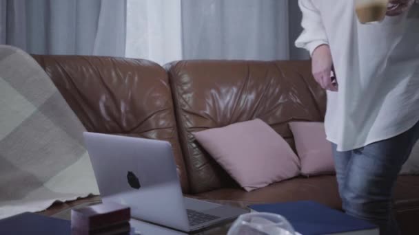 Madura sonriente mujer caucásica que viene con capuchino a la computadora portátil y mirando a la pantalla. Jubilados mayores navegando por Internet en casa. Pasatiempo, ocio, redes sociales . — Vídeos de Stock