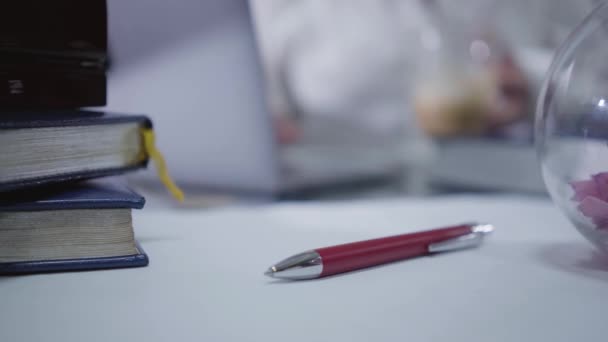 Close-up of red pen laying at the table. Blurred Caucasian woman using laptop at the background. Intelligent lady with coffee cup surfing internet at home. Social networks, pastime. — Stock Video