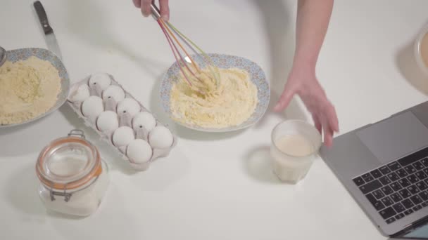 Вид сверху на смесь муки с яйцом и молоком. Женщины-белые руки используют венчик, чтобы смешивать ингредиенты для пекарни. Домохозяйка готовит дома. Хобби, досуг . — стоковое видео