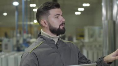 Sakallı beyaz adam depoda hazır üretim sayıyor ve miktarı kontrol ediyor. Çelik fabrikasında kendine güvenen erkek işçiye yakın çekim. Üretim, endüstri, depo.