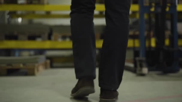 Kamera efter manliga ben kommer till stål plåtlager och tar en sak. Arbetare vid stålproduktionsanläggningen. Tillverkning, industri, anläggning, godsterminal. — Stockvideo