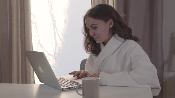 Evinde internette sörf yapan beyaz bir kızın portresi. Güzel esmer kadın dizüstü bilgisayar kullanıyor ve ekrana bakıyormuş gibi surat yapıyor. İnternet, internet, sosyal medya. — Stok video