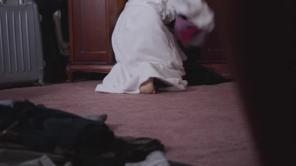 Bottom view of female Caucasian legs in front of bathrobe. Young woman in white bathrobe throwing clothes on floor, running away, Hurrying girl choosing outfit. Focus changes from person to stuff. — Stock Video