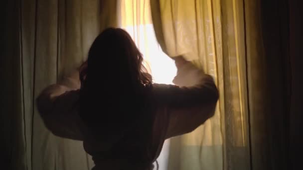 Visão traseira da morena caucasiana mulher cortinas de abertura e olhando para fora da janela pela manhã. Retrato de menina bonita em raios de sol. Felicidade, prazer . — Vídeo de Stock