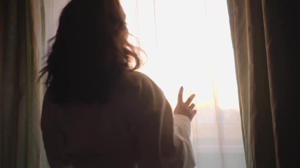 Profiel portret van een lachend gelukkig meisje dat 's morgens in de zon staat. Positieve jonge blanke vrouw die thuis uit het raam kijkt. Vroege ochtend, geluk, levensstijl. — Stockvideo