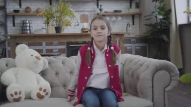 Kamera, beyaz oyuncak ayıyla kanepede oturan gülümseyen esmer beyaz kıza yaklaşıyor. Örgü örgülü at kuyruğu ve kahverengi gözlü güzel genç bir çocuğun portresi. Çocukluk, güzellik, rahatlık..
