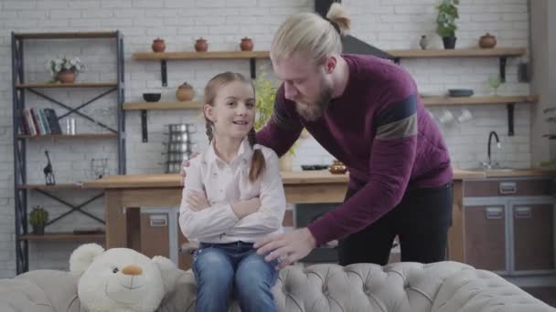 Close-up of little teenage girl with braided pigtails sitting on sofa and talking with bearded father. Happy daughter spending time with parent indoors. Leisure, lifestyle, family. — Stock Video