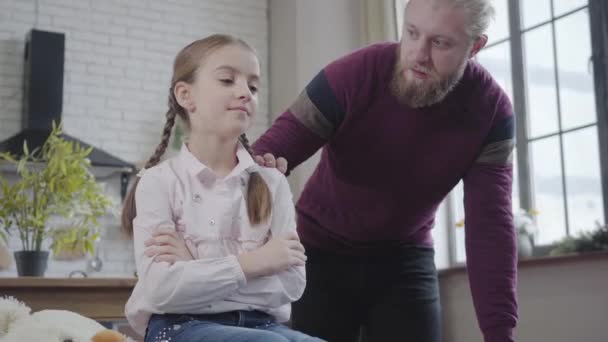 Portrait of upset Caucasian teenage girl sitting with hands crossed as adult man talking to her at the background. Father helping his daughter to solve problems. Care. parenthood, adolescence. — ストック動画