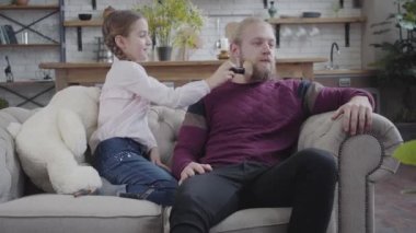Makyaj fırçası alıp babasının sakalını tarayan beyaz, tatlı bir kız. Üzgün adam kızlarının elini itiyor. Genç adam üzgün yetişkin adamı neşelendiriyor..