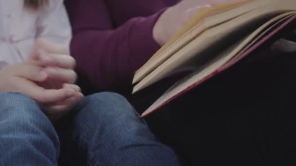 Hombre caucásico adulto y adolescente sentado con libro. Mano masculina volteando páginas, hija agarrada de rodillas. Educación, hobby, lectura, inteligencia . — Vídeo de stock