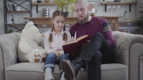 Bonito homem caucasiano a virar páginas de livros e a falar com uma adolescente. Filha rindo como ouvir o pai. Paternidade, educação, hobby . — Vídeo de Stock