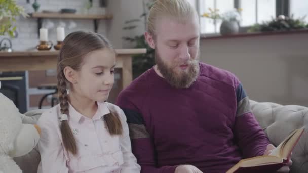 Zijaanzicht close-up van blanke man lezen boek en aanraken dochters neus. Mooie vrouwelijke tiener die samen met vader lacht. Ouder die zijn kind thuis opvoedt. Plezier, hobby, levensstijl. — Stockvideo