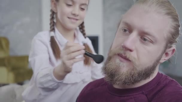 Retrato de close-up do jovem homem caucasiano exausto empurrando as filhas mão como menina adolescente pentear sua barba com pincel de maquiagem. Adolescente a incomodar o pai. Adolescência, relação . — Vídeo de Stock