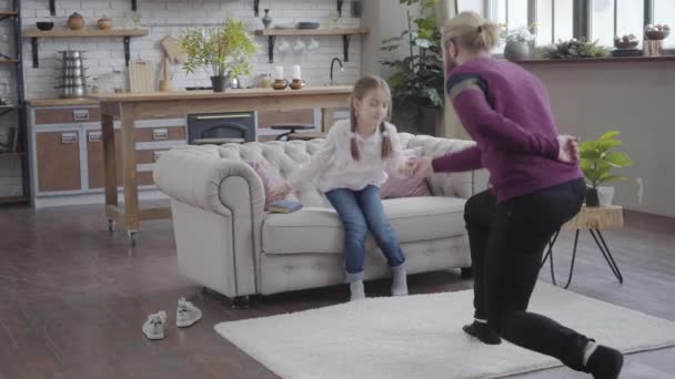 Volwassen blanke vader die op één knie staat en dochters vasthoudt. Een tienermeisje die een boek opbergt en met vader danst. Vrolijke familie die samen tijd doorbrengt. Camera nadert meisje. — Stockvideo